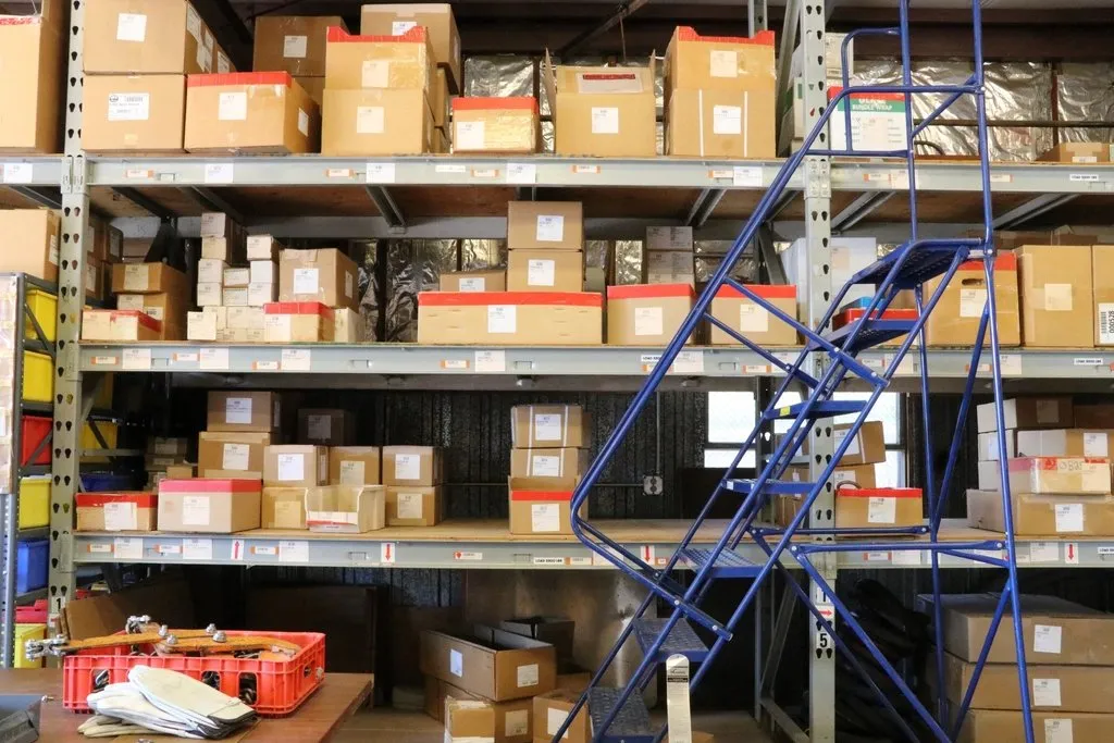 Rak gudang berisi kardus barang dengan tangga beroda