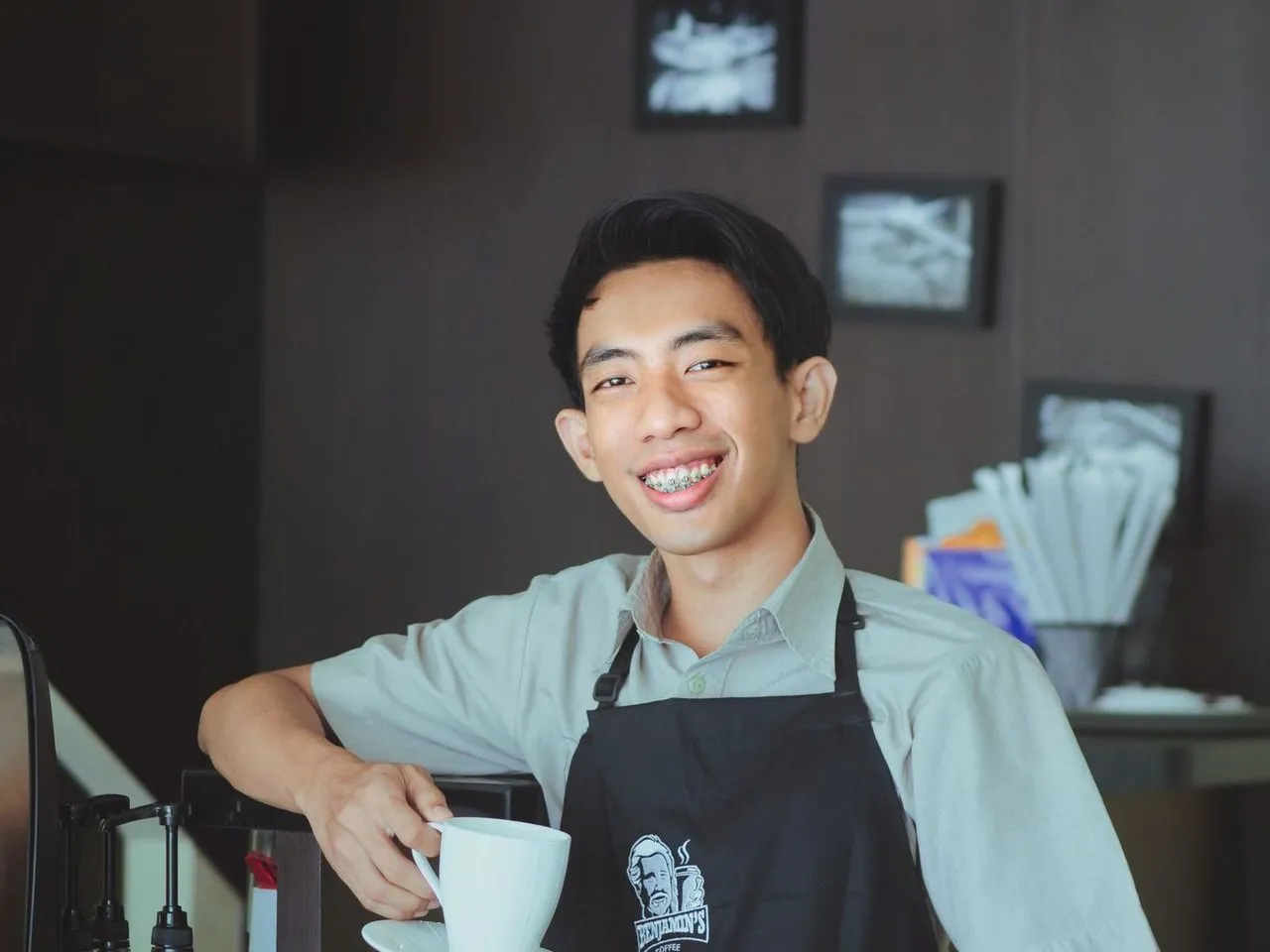 Barista tersenyum memegang cangkir kopi