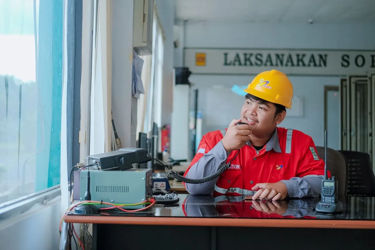 Pekerja berhelm kuning berbicara lewat radio di ruang kendali