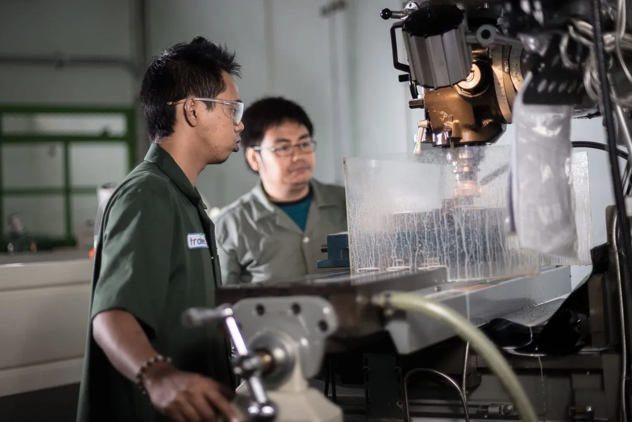 Dua teknisi mengoperasikan mesin CNC di bengkel