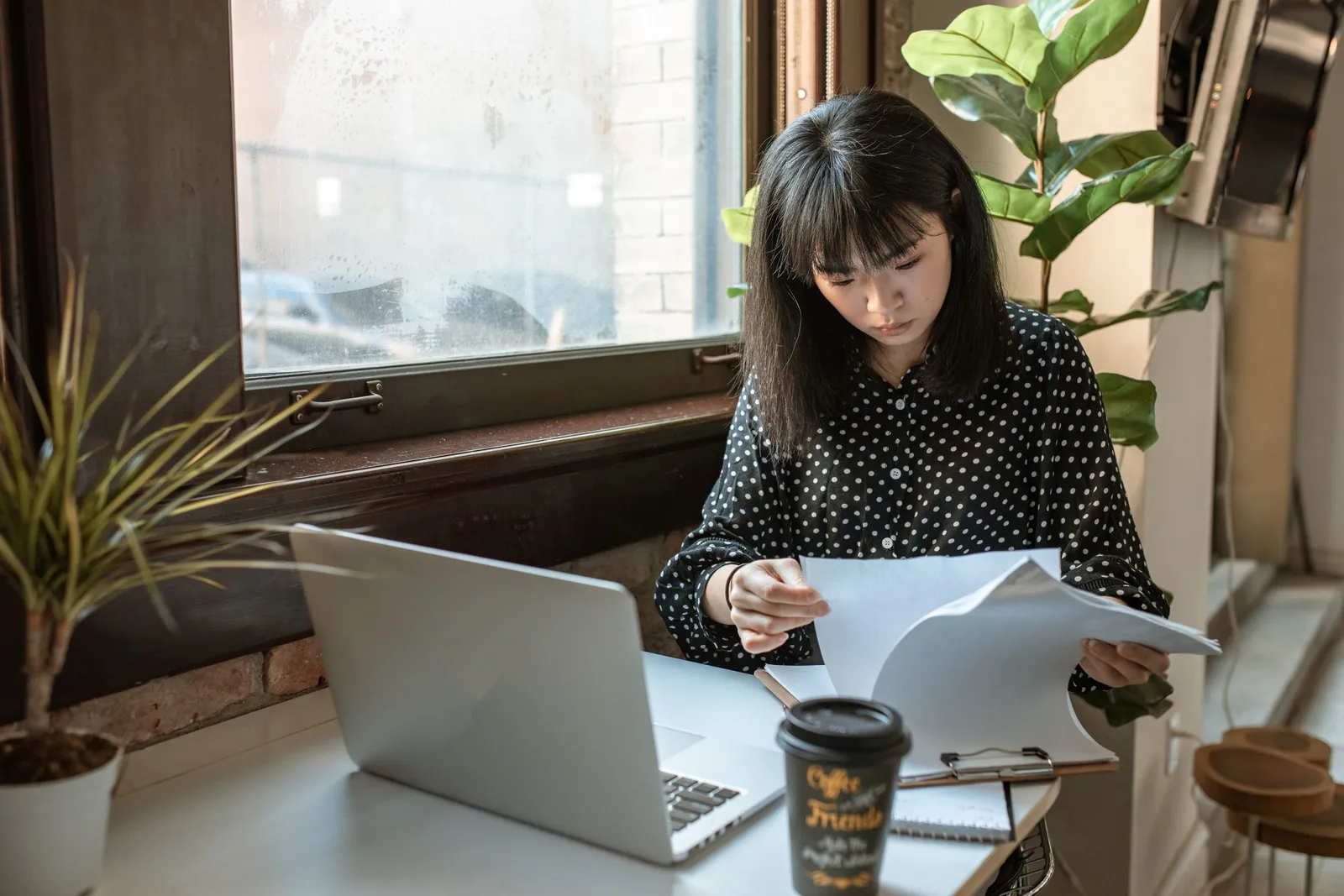 Perempuan membaca dokumen di samping laptop