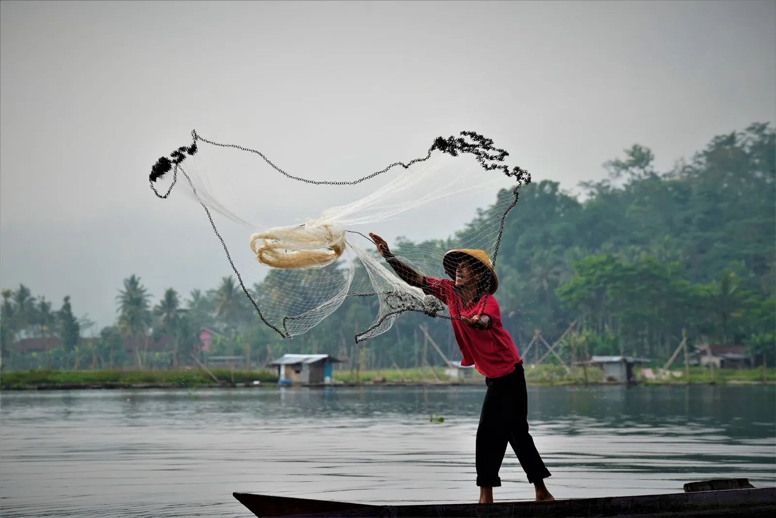 Nelayan menebar jala dari perahu