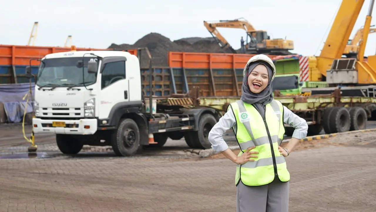 Pekerja berhijab dan berhelm di area tambang dengan truk dan ekskavator