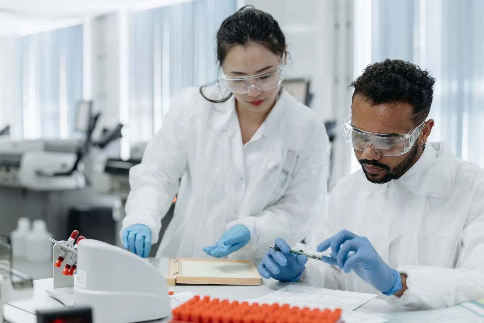 Dua peneliti berjas lab menganalisis sampel di laboratorium