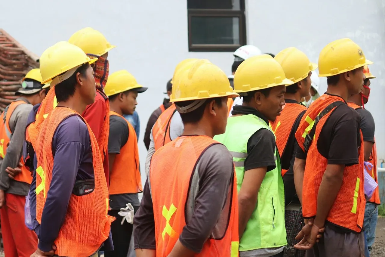 Pekerja proyek berhelm kuning dan rompi keselamatan berkumpul di lokasi proyek