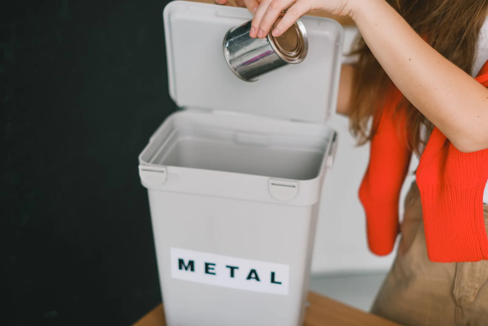 Tangan memasukkan kaleng ke tempat sampah berlabel logam