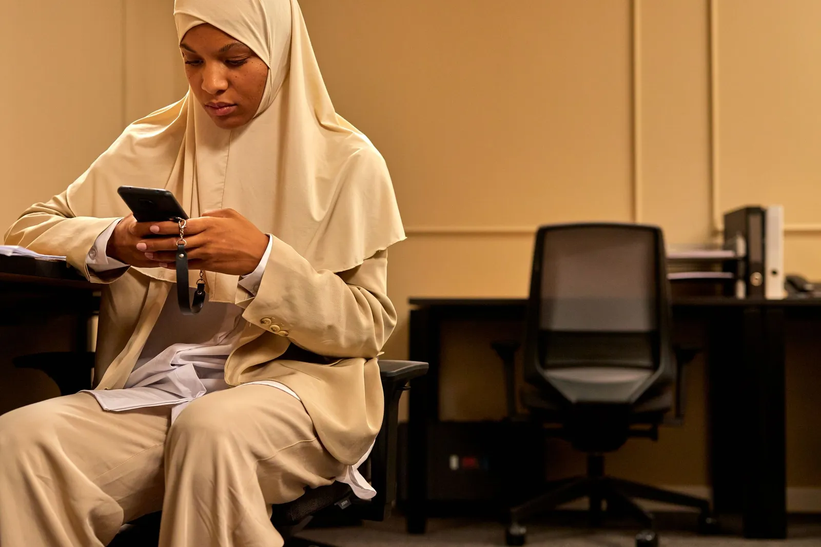 Perempuan berhijab memeriksa ponsel di kantor