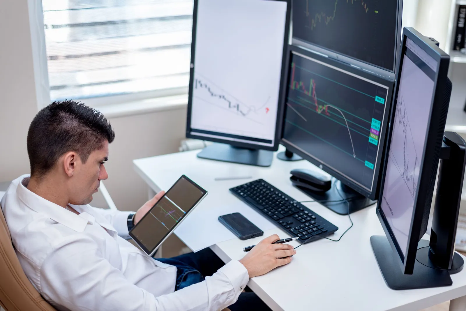 Analis memeriksa grafik di beberapa monitor sambil memegang tablet