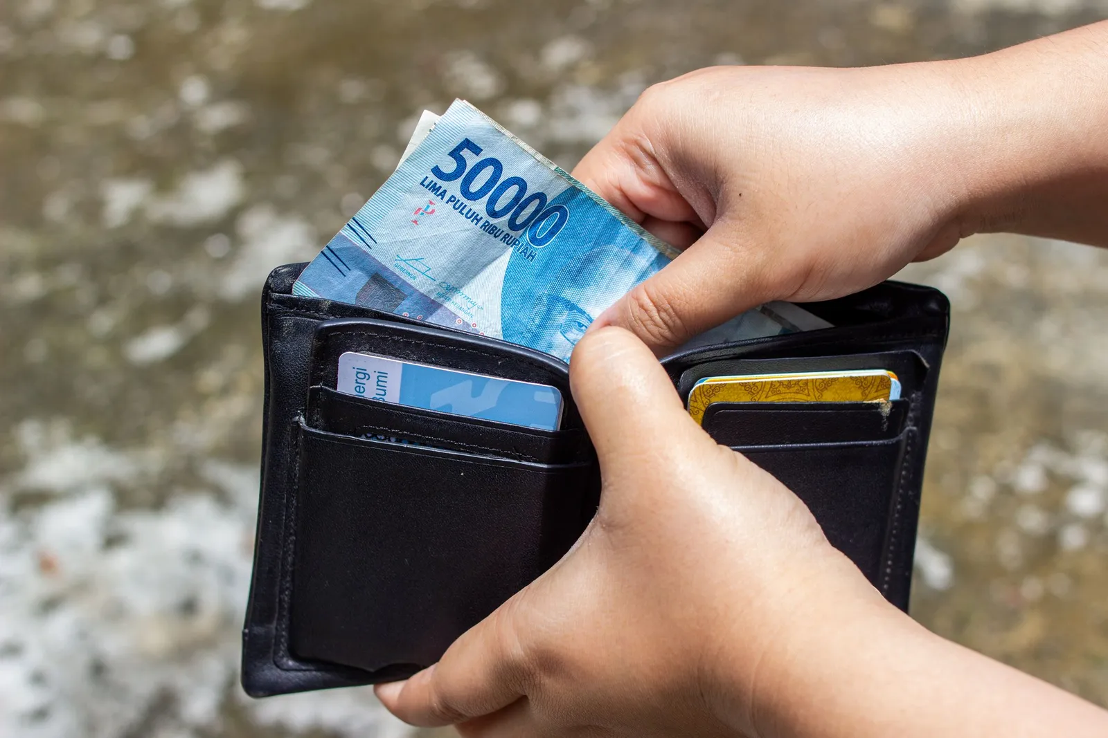 Tangan memasukkan uang rupiah ke dompet hitam