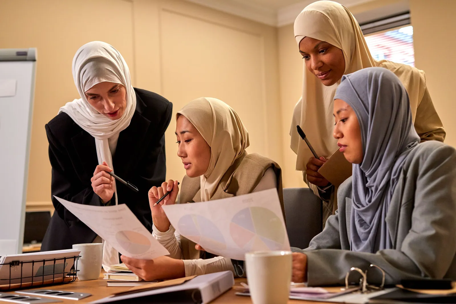 Karyawan berhijab berdiskusi sambil meninjau dokumen