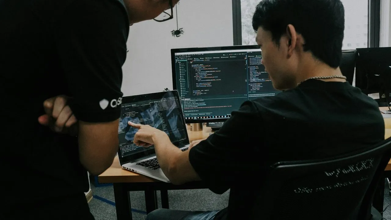 Dua programmer berdiskusi di depan layar kode