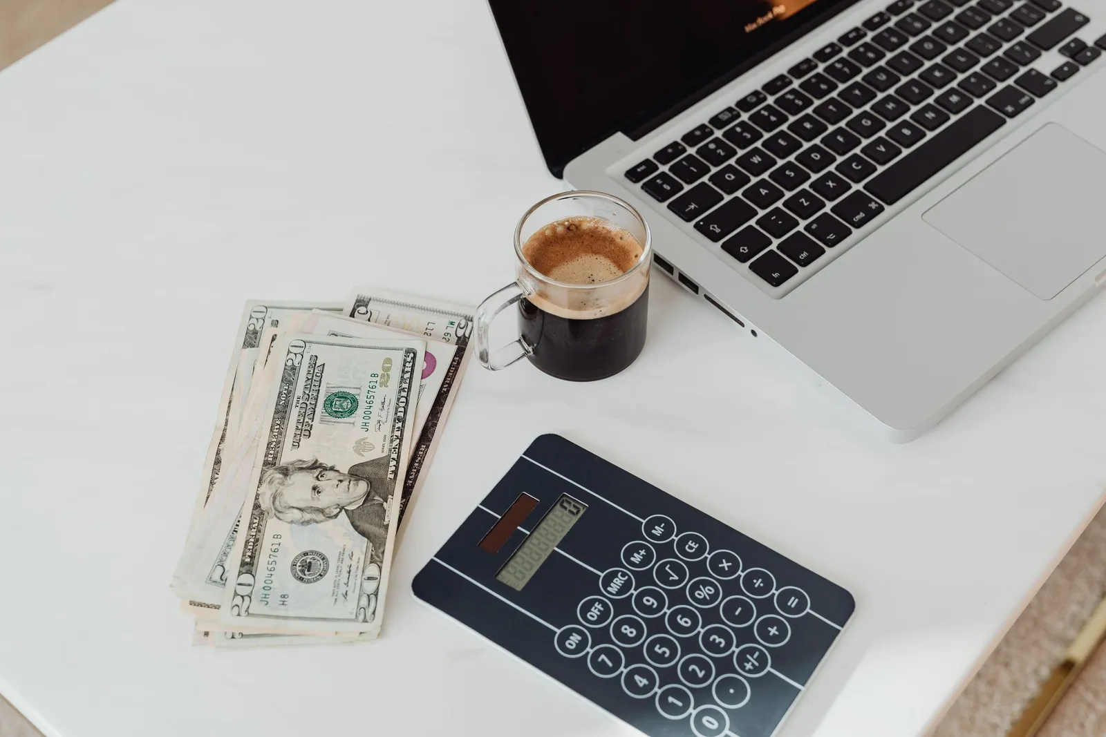 Uang, kopi, kalkulator, dan laptop di meja kerja