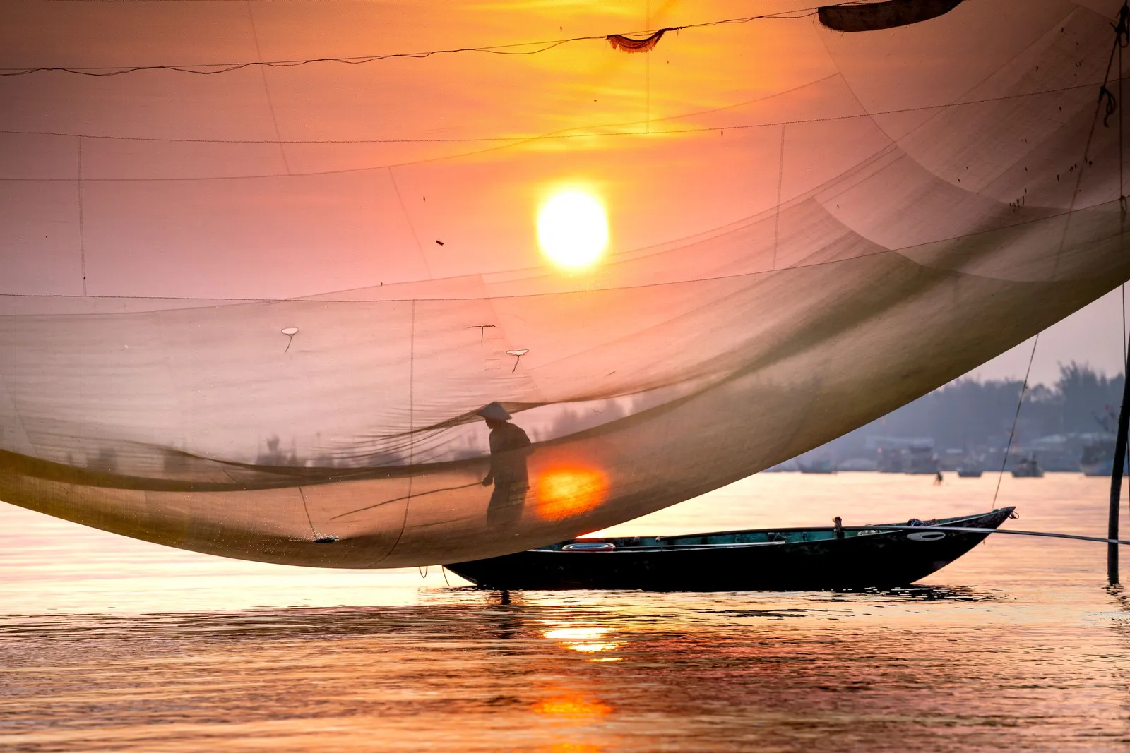 Nelayan dengan jaring di perahu saat matahari terbit