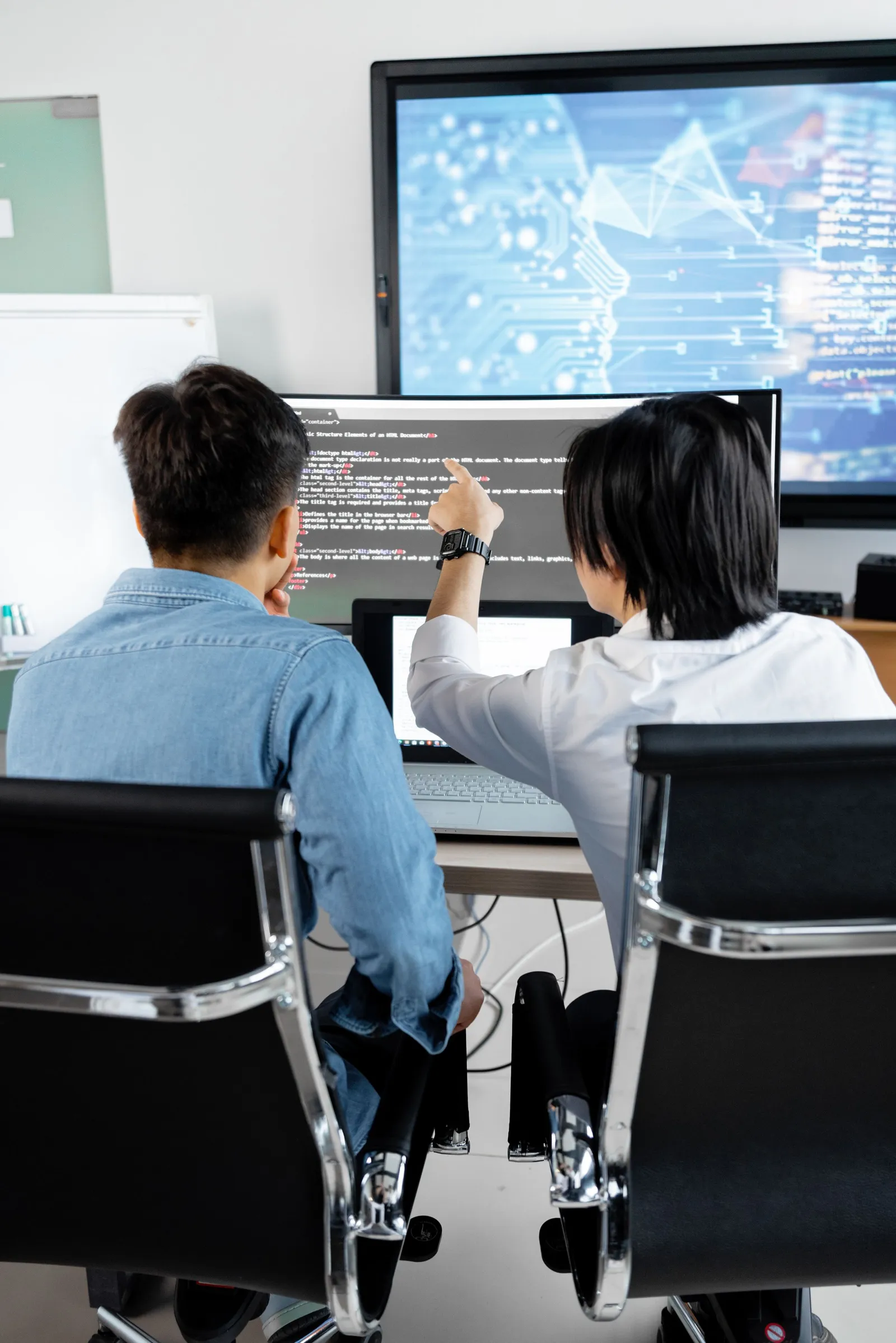 Pengembang menunjuk kode di monitor sambil berdiskusi